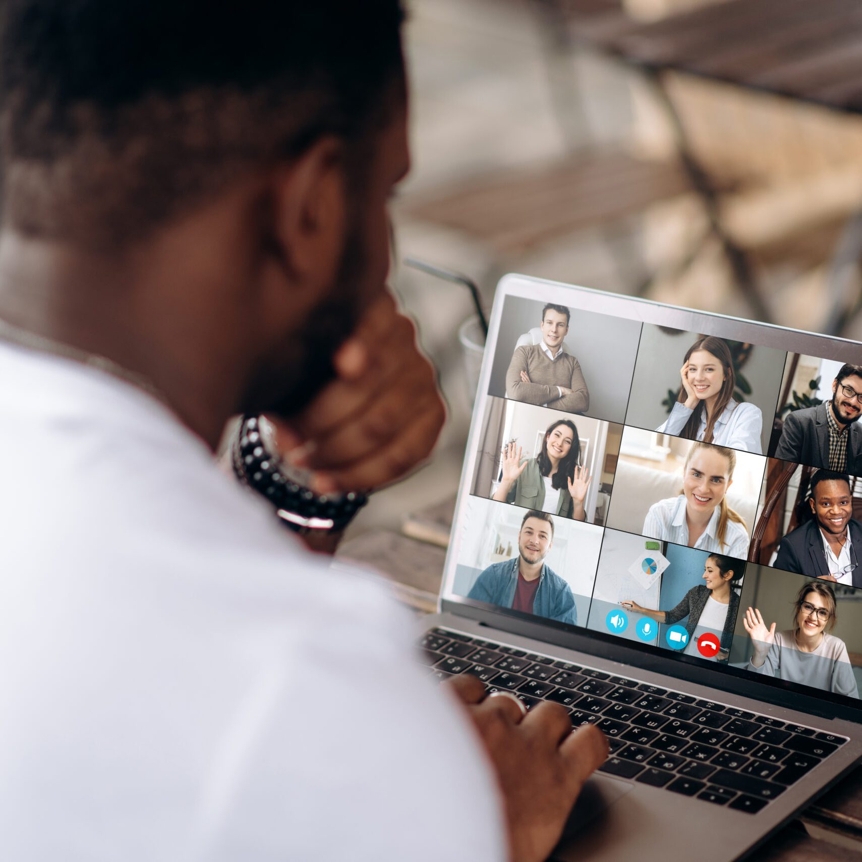 Video call. Online business meeting. Successful African American freelancer communicate by a video conference with his colleagues using a laptop while sitting in cafe in a summer terrace, they discussing about business affairs. On a laptop screen, participants of a video conference
